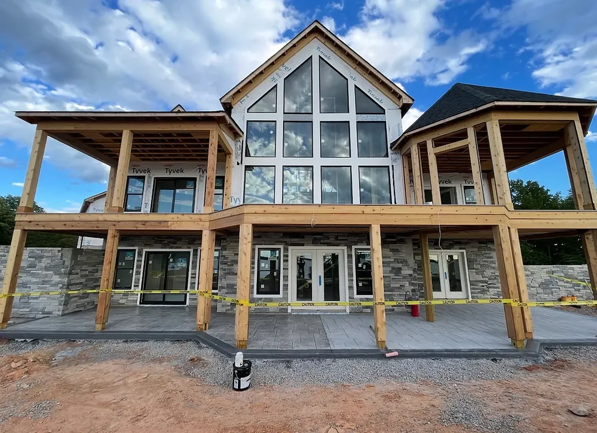 A Legasea waterfront custom home with a tall glass gable, stone base and two levels of decks, nearing completion