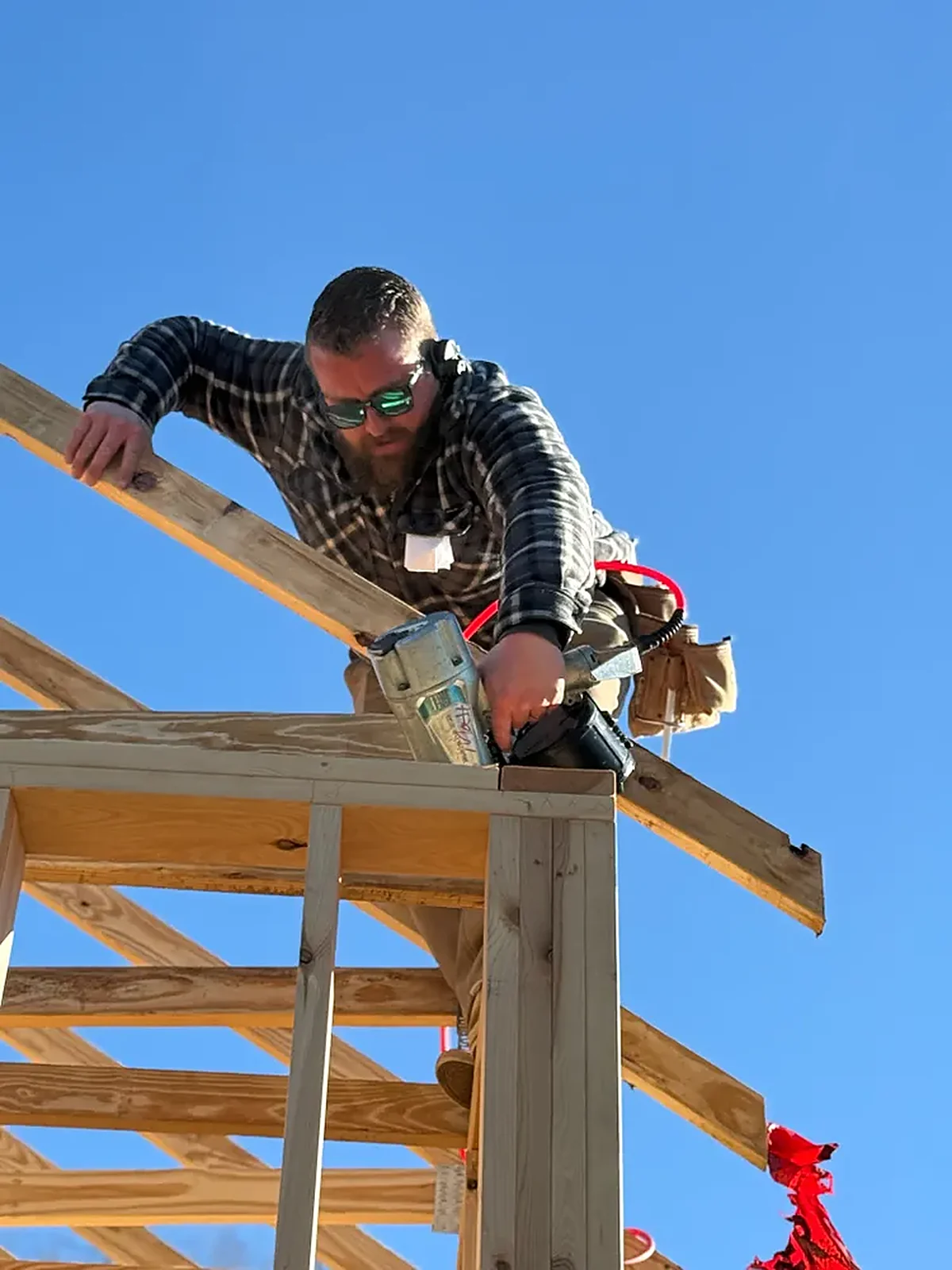Matt Self, owner of Legasea Construction, framing a roof against a blue sky