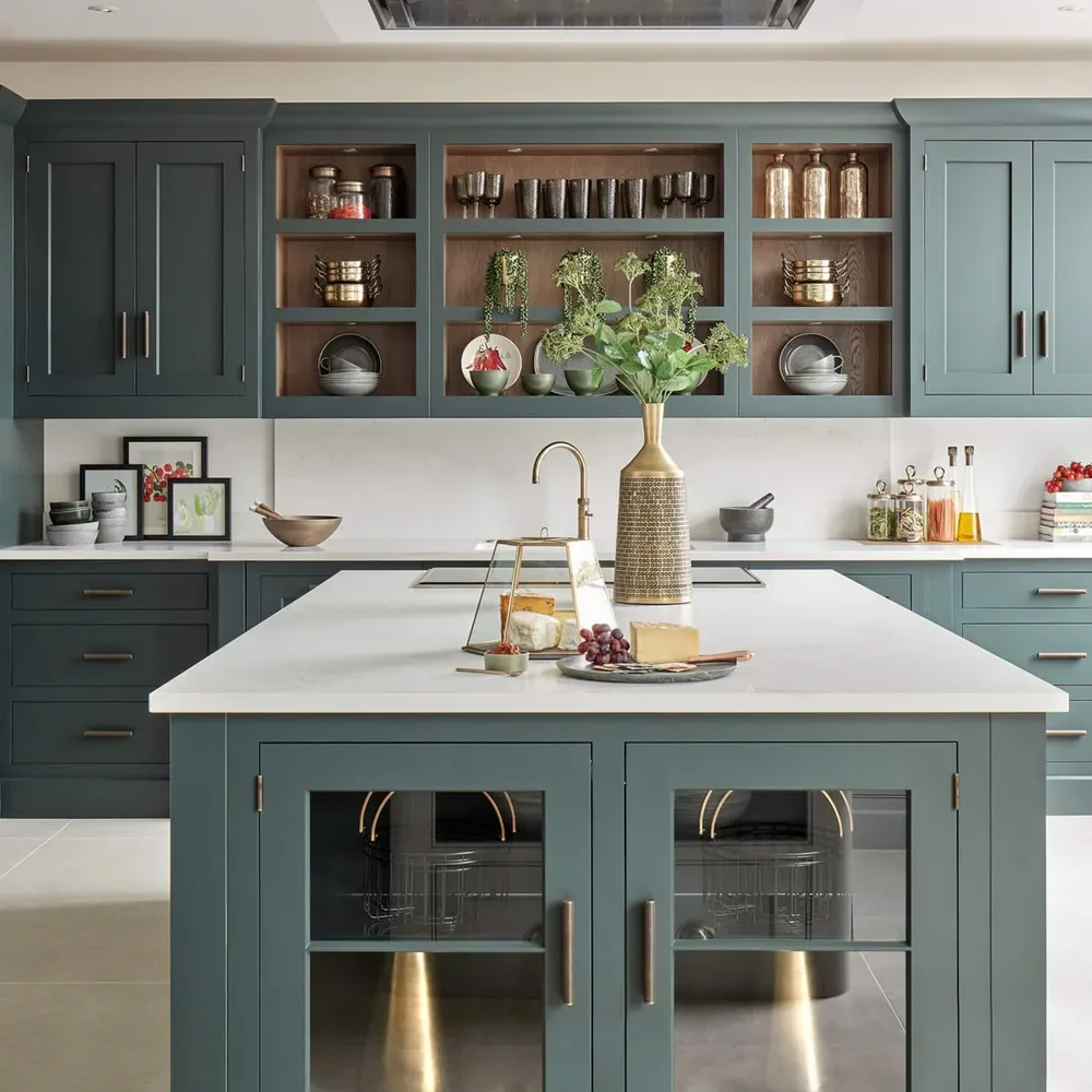 A kitchen with sage green cabinets, open shelving and a marble-topped island