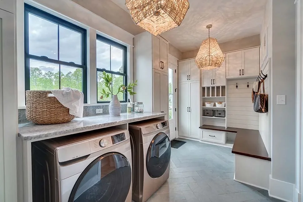 A laundry room with front-load machines, cabinetry and a mudroom bench